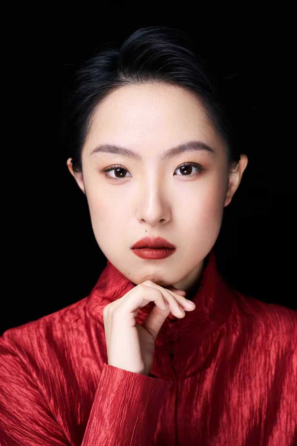Xiaoru Wen in a red silk jacket, chin resting on one hand